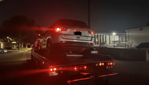 Gray car being towed at night on flatbed tow truck in Fullerton California