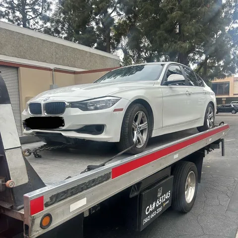 Flatbed tow truck carrying stalled white car in Cerritos, California daytime