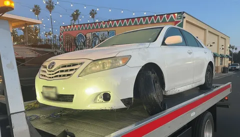 White car being towed on flatbed tow truck in Los Alamitos California daytime