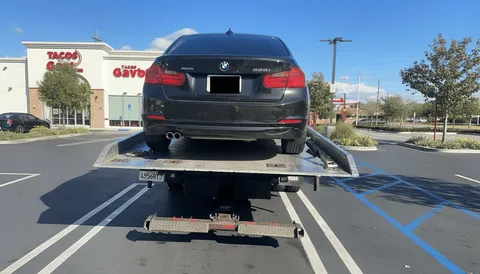 Black car on tow truck during daytime roadside service in La Palma California