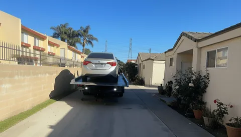White car being towed on flatbed tow truck daytime in Stanton California
