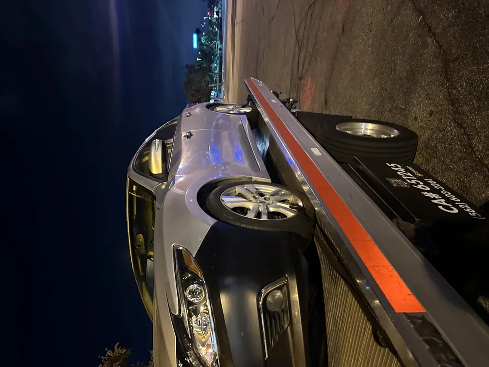 Carsaad Towing flatbed picking up a stalled sedan at night in Artesia, California.