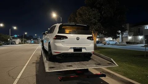 White car being towed evening on flatbed tow truck in Santa Fe Springs California.