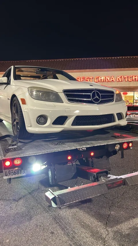 Flatbed tow truck transporting broken down car in Bell Gardens California
