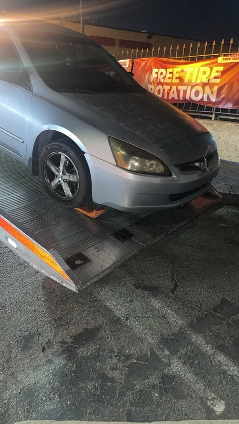 Tow truck lowering a stalled sedan onto the ground in Artesia, California.