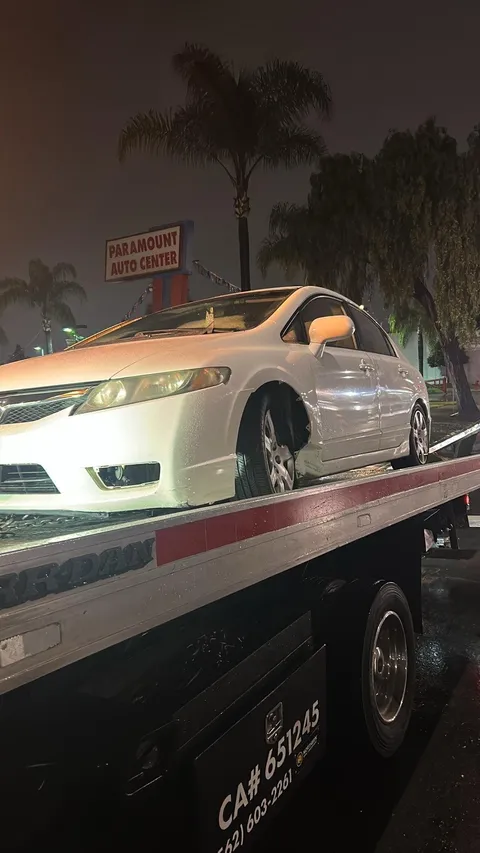 White vehicle securely loaded on a flatbed tow truck for safe transport in Downey, California.