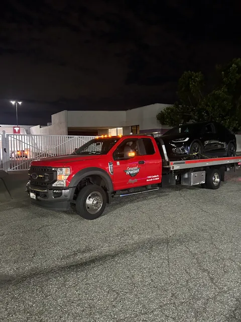 Red flatbed tow truck towing a black Tesla Model X in Anaheim, CA on