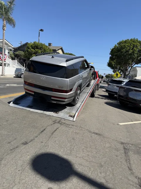 Carsaad Towing flatbed tow truck loading a gray Hyundai Sonata on a flatbed in suburban Bellflower, CA