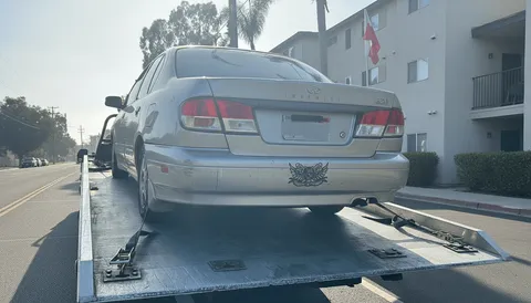Gray car being towed on flatbed tow truck morning in Seal Beach California