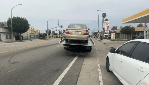 Beige car on flatbed tow truck on highway in La Mirada California morning