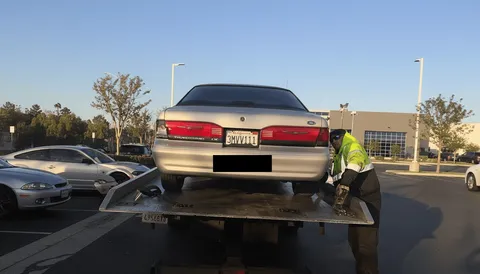 White car being towed on flatbed tow truck morning in Santa Fe Springs California