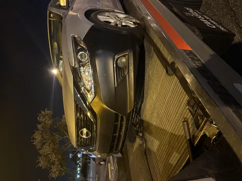 Black sedan getting unloaded from flatbed tow truck at night in Hawaiian Gardens California