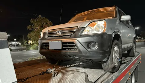 Gray Honda secured on flatbed tow truck at night in Orange County California