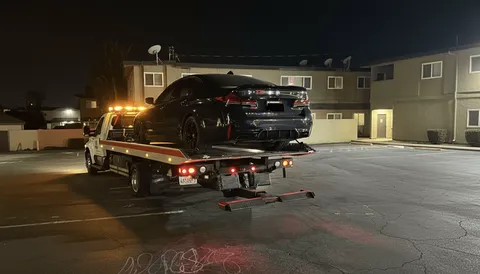 Black car on tow truck at night in parking lot in La Mirada California