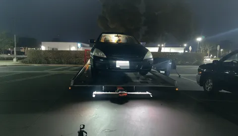 Black car getting unloaded from flatbed tow truck at night in Fullerton California