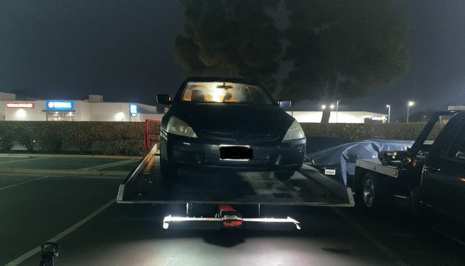 Black car being unloaded from tow truck at night in Santa Fe Springs California