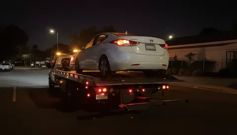 White car secured on tow truck at night in Montebello California