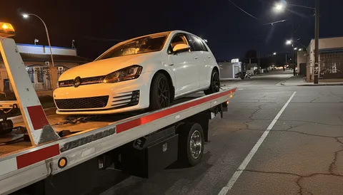 White car being towed on flatbed tow truck at night in Seal Beach California