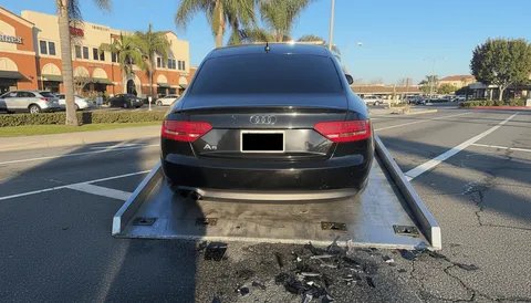 Black car secured on tow truck during daytime in Pico Rivera California