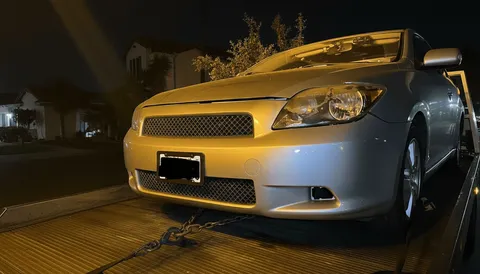 Gray car secured on a tow truck during nighttime roadside assistance in South Whittier, California.