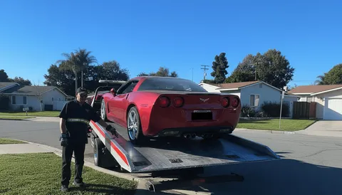 Red car being towed from backyard on flatbed tow truck in West Whittier California