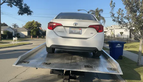 Tow truck transporting broken-down white car in Cerritos CA daytime